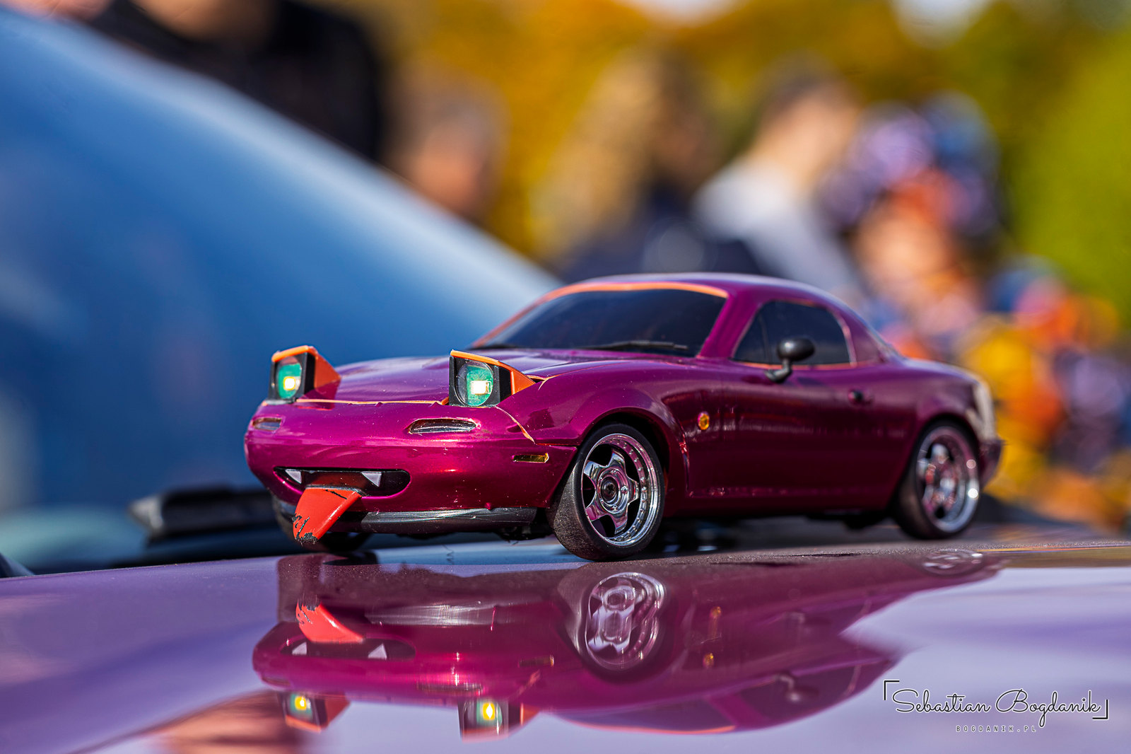 Two Miatas: a real one with pop-up headlights, and a toy one with sleepy eyelids and its tongue out (2/2)