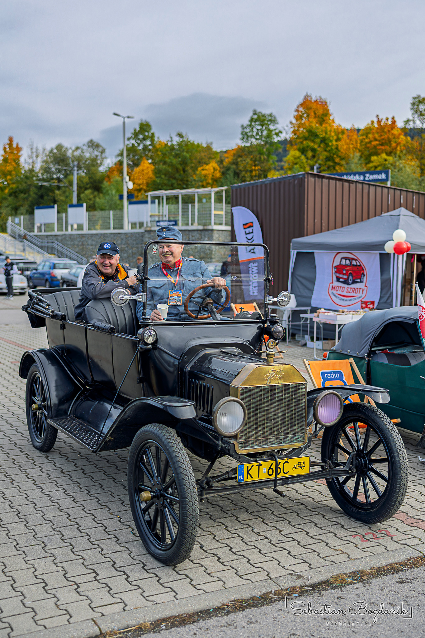 A black Ford Model T with a brass radiator and an open body, two people inside.