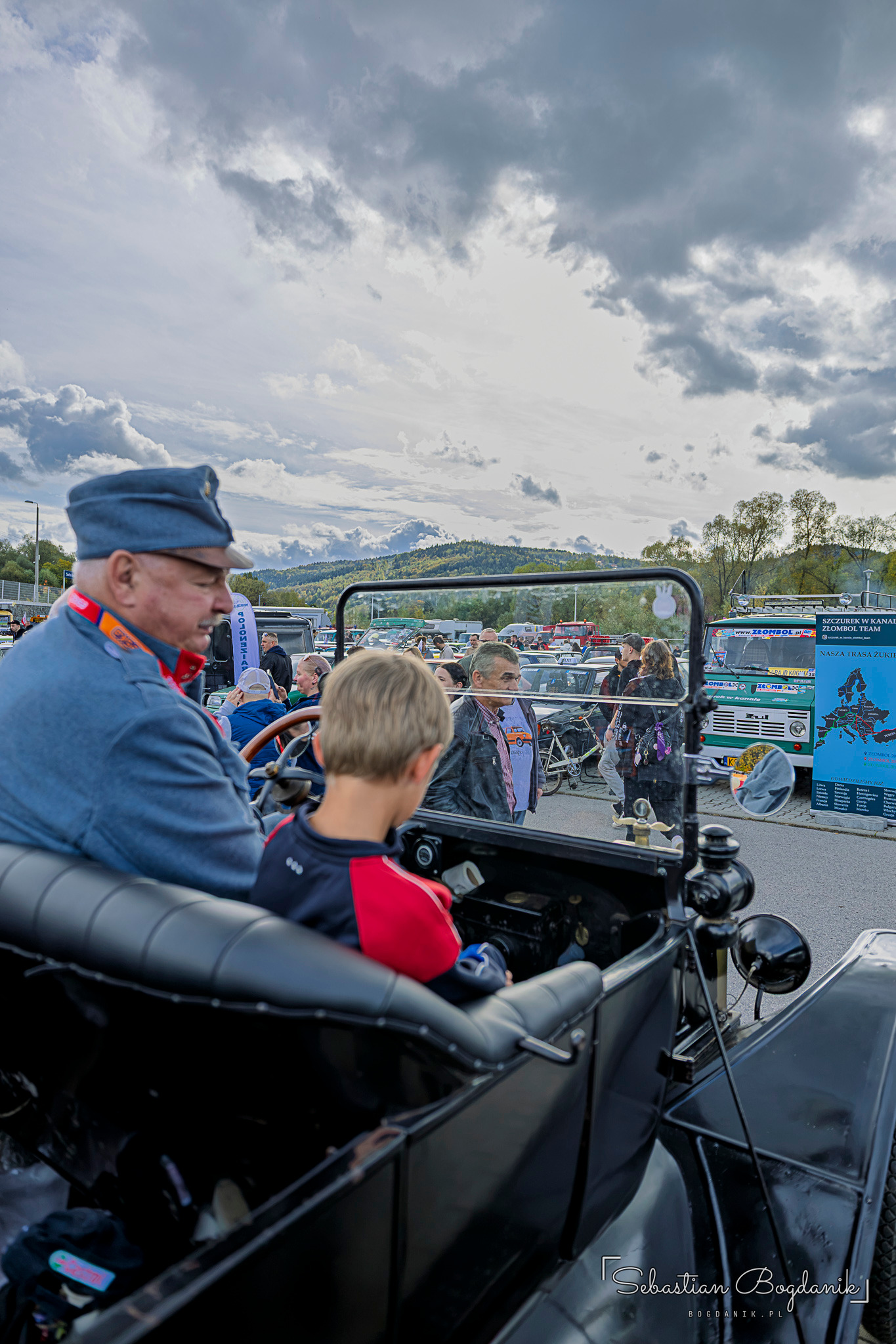 A man in a period uniform and a child in the front seats of an open vintage car.