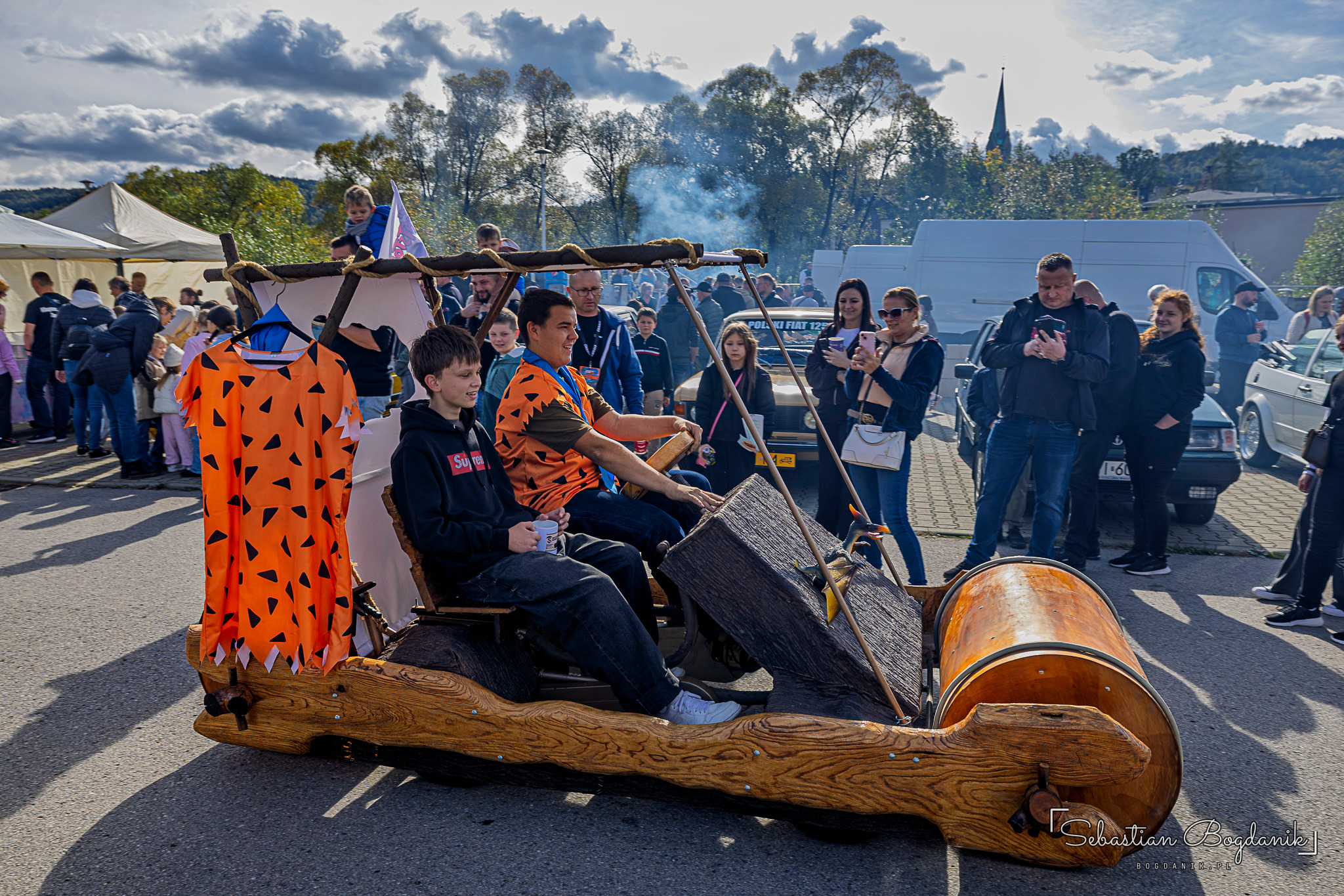 A wooden replica of the cartoon car with rollers instead of wheels, people sitting in it and an orange costume hanging alongside.