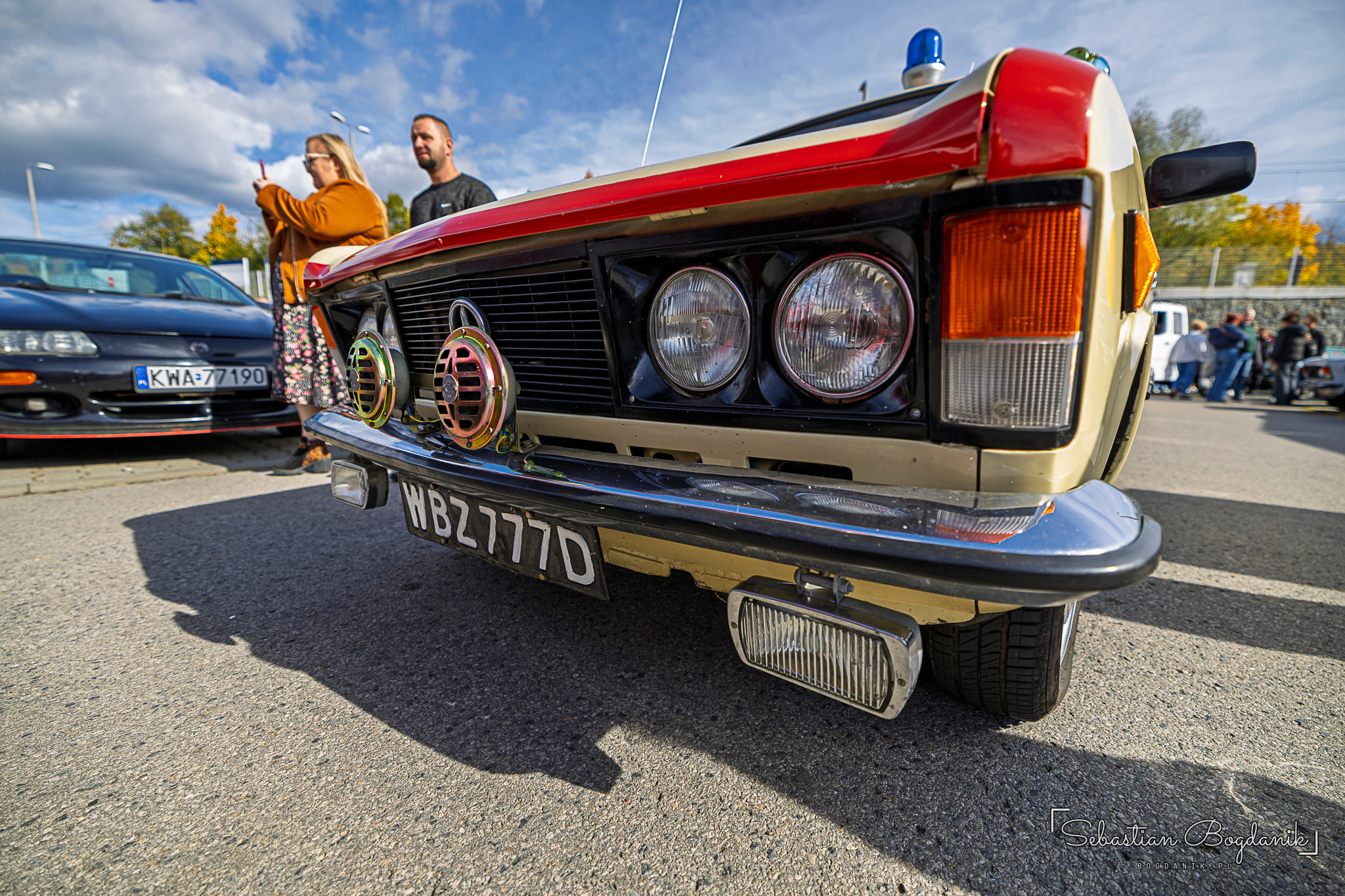 The front of a beige FSO 125p with a red stripe, round headlights and old black number plates.