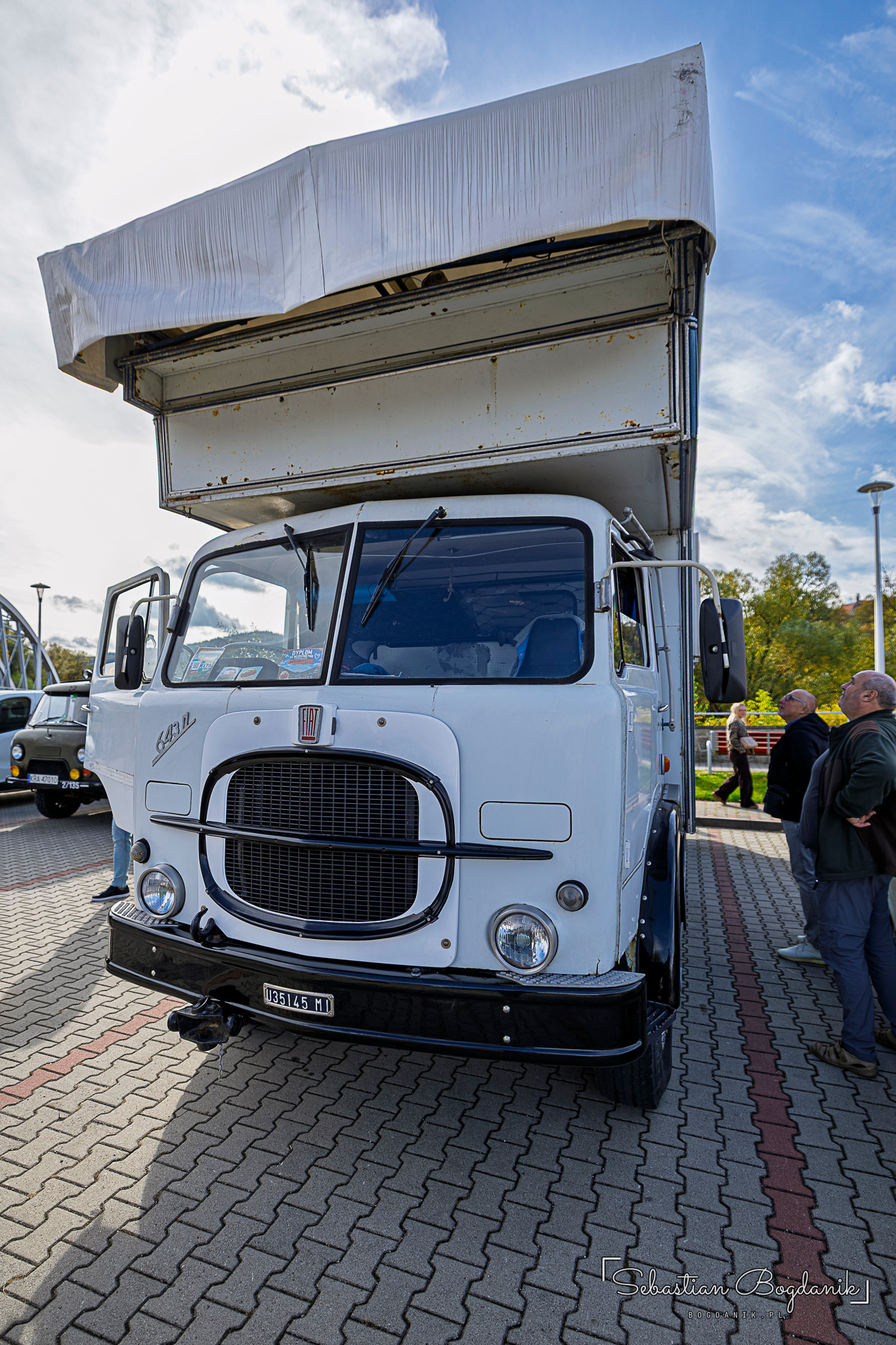 A white Fiat truck with a large grille and a wood-and-white living compartment on the chassis.